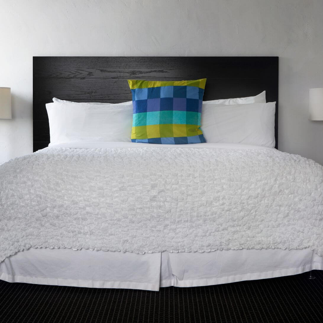 Opgemaakt bed met wit beddengoed en groen geblokte kussen
