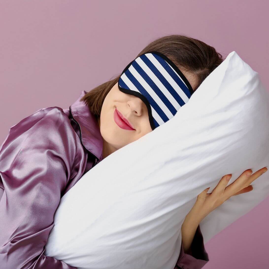 Vrouw met slaapmasker houdt wit hoofdkussen tegen haar hoofd