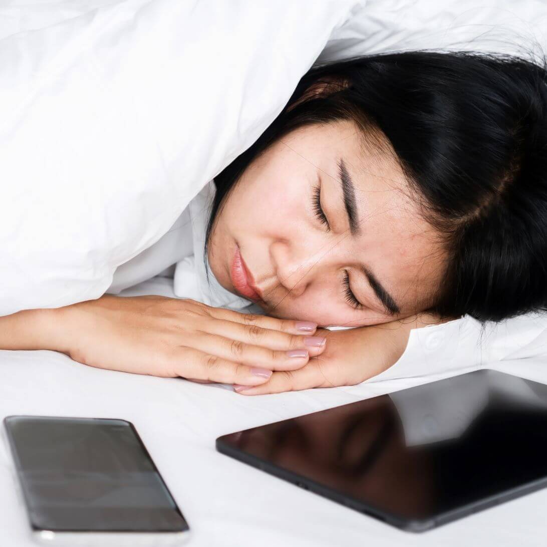 Vrouw ligt in bed te slapen naast haar telefoon en tablet