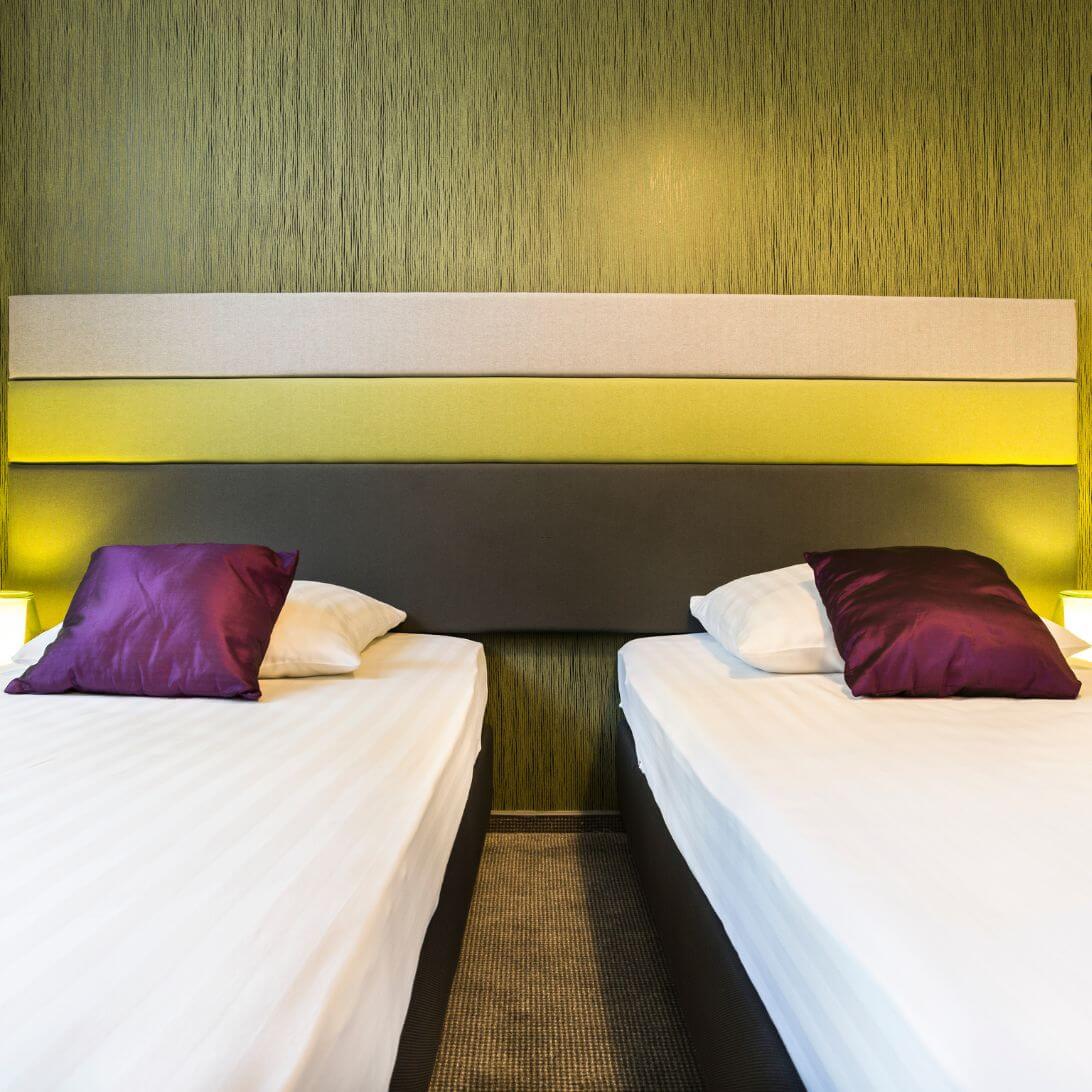 Twee losse bedden met wit beddengoed en een paars kussen, in een groene slaapkamer