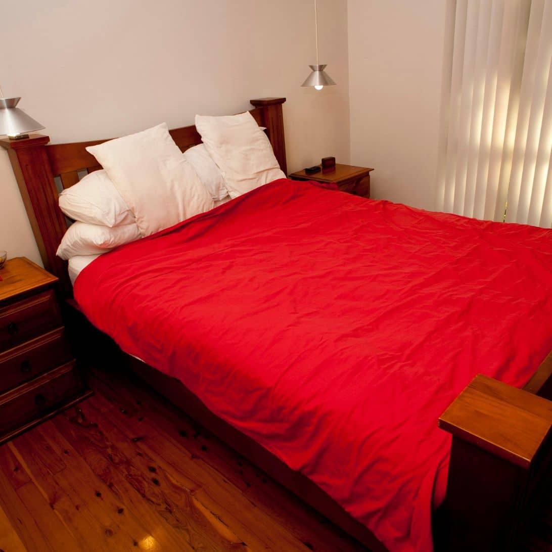 Houten bed, opgedekt met rood beddengoed en witte kussens