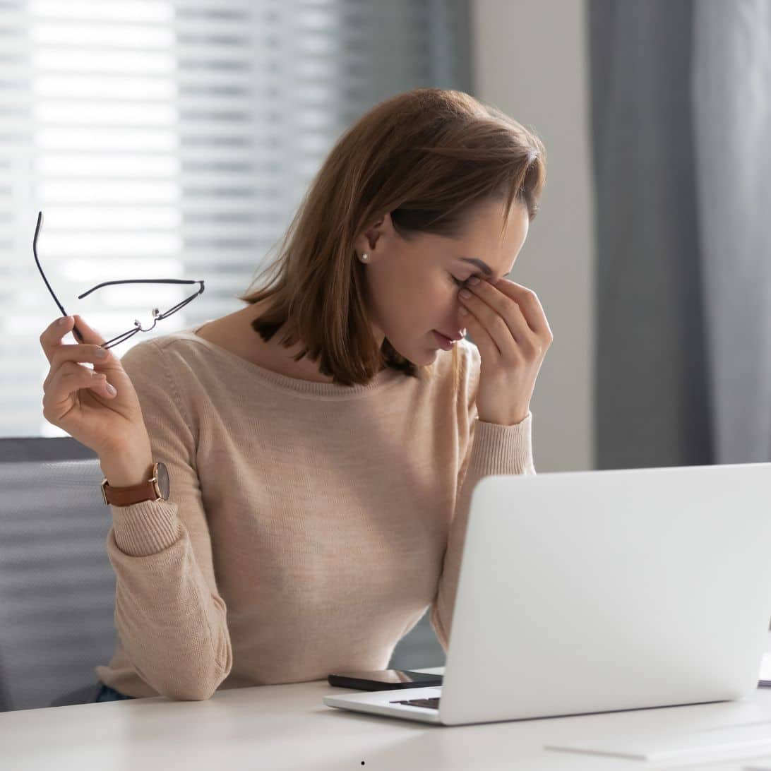 Vrouw achter laptop met bril in hand die niet genoeg slaap heeft