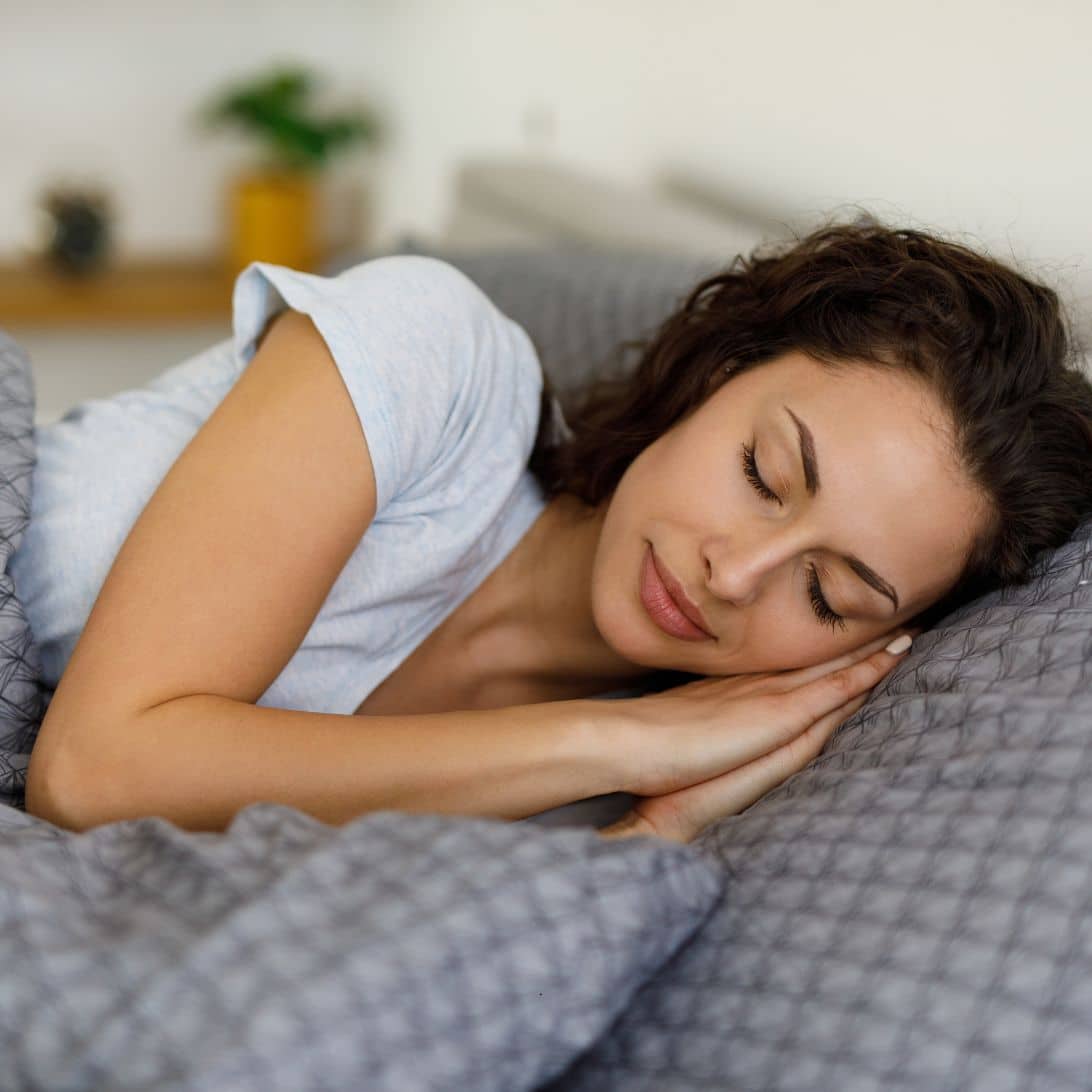 Vrouw met een grijze deken en kussen die slaapkwaliteit wilt verbeteren