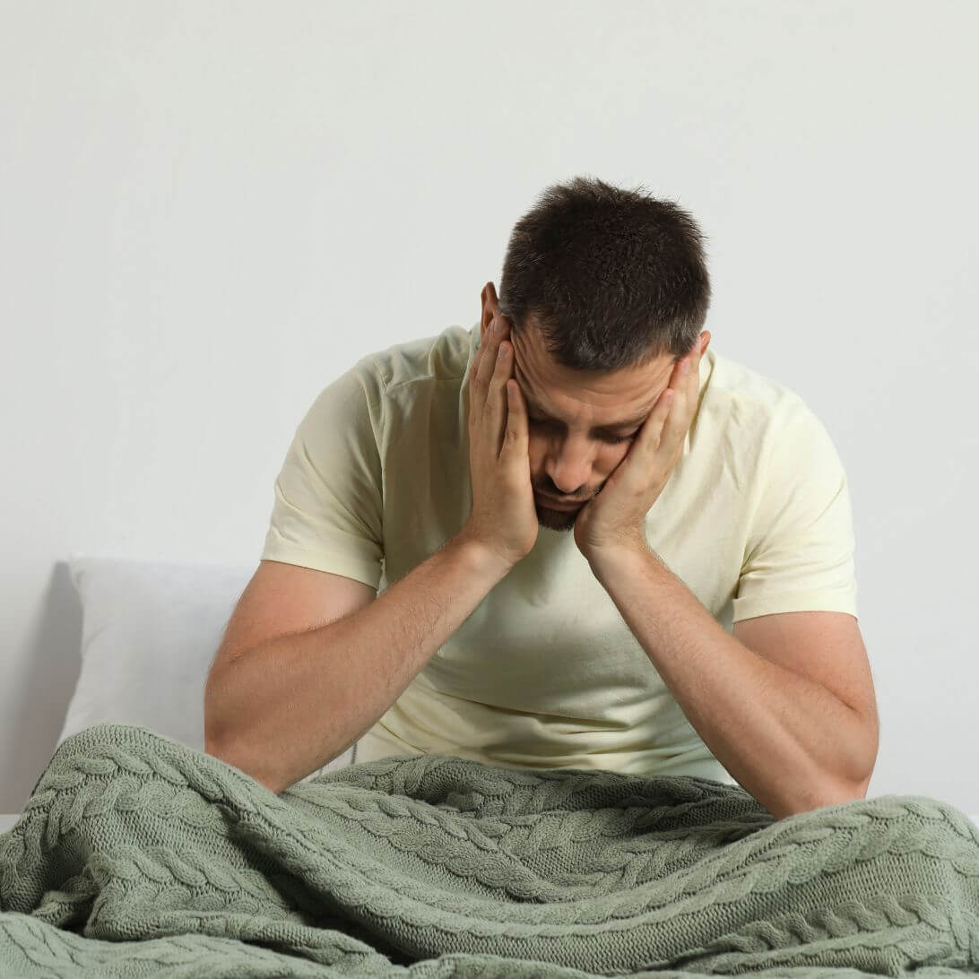 Man met slaapgebrek zit op bed met hoofd in handen