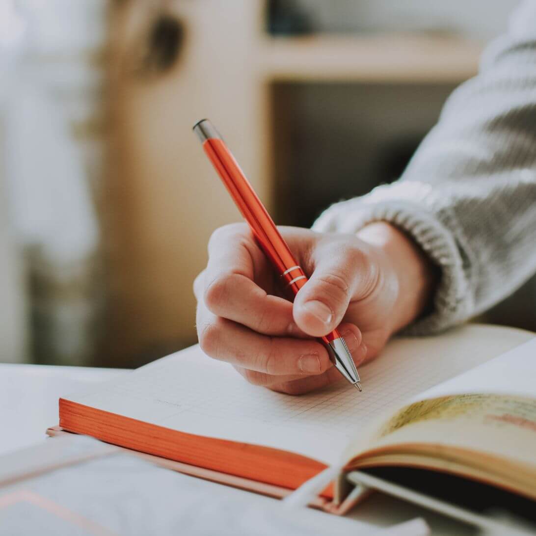 Hand met pen boven een boek