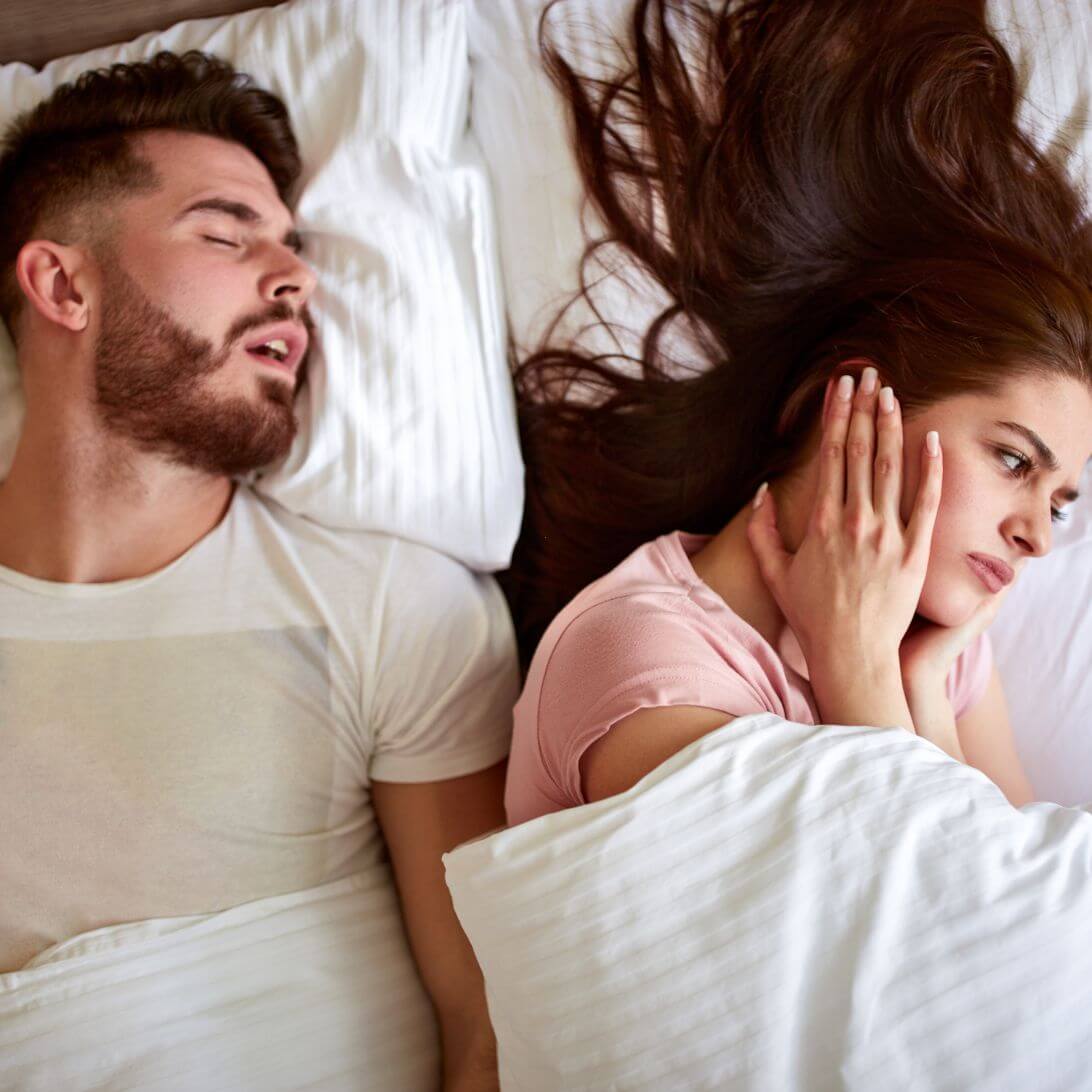 Vrouw heeft handen over oren naast partner die aan het snurken is