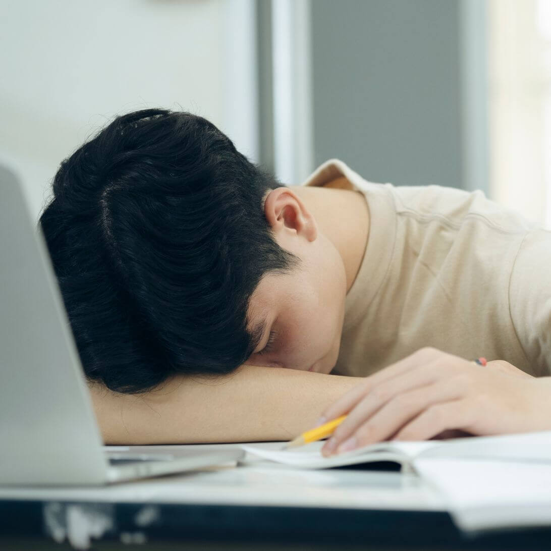 Een student slaapt op zijn bureau gevuld met zijn laptop en studieboeken