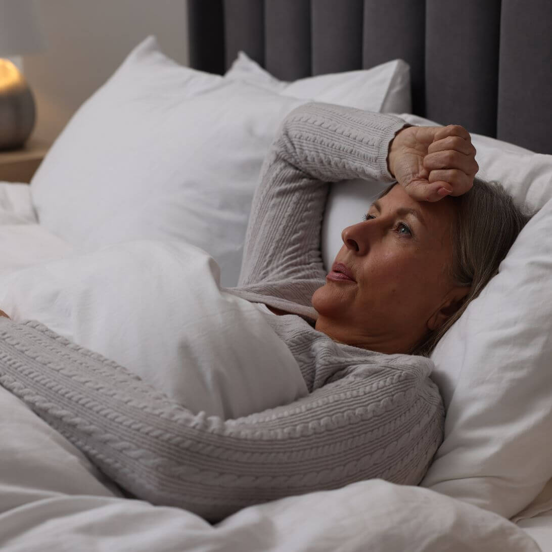 Vrouw in grijze pyjama heeft het warm en kan niet slapen tijdens warme zomernacht